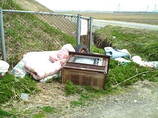 道端に、布団や古いテレビなどが不法投棄されている写真