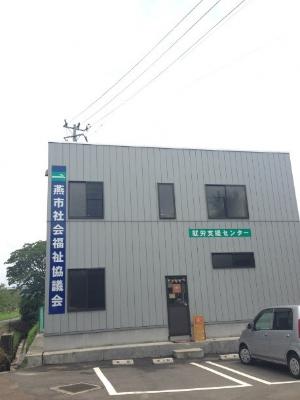 前に駐車場があり2階建ての灰色の外壁で大きな窓がある就労継続支援A型・就労継続支援B型燕市社会福祉協議会就労支援センターの外観写真