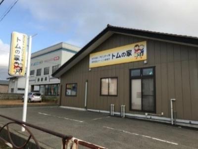 焦げ茶色の外壁で外壁と通りに面して外側に看板がある生活介護・就労継続支援B型NPO法人アビリティ燕トムの家の建屋外観写真
