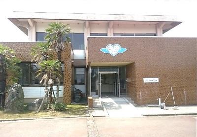 青い屋根で茶色い外壁でエントランス前に植え込みがある就労継続B型あいこうえん翼の建屋外観写真
