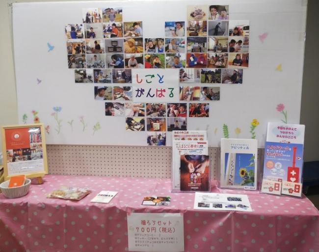 燕市内事業所で、障がいのある方々が生き生きと笑顔で仕事をがんばる様子の写真を白番にハートの形に貼って展示している写真