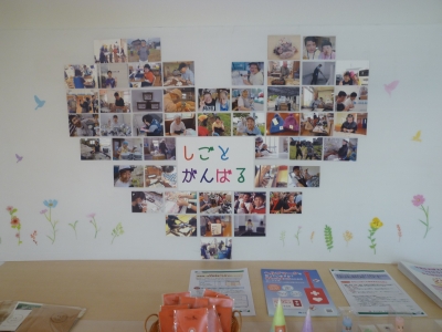 「しごとがんばる」の文字と共に全体がハートマークになるように壁に貼られているたくさんの写真