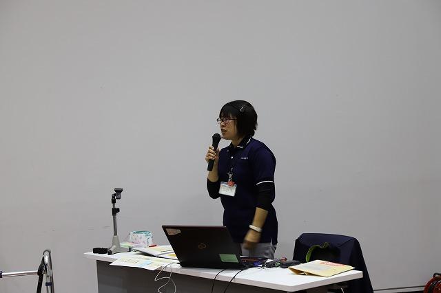 歩き方講座で立ったままマイクを使い説明をする眼鏡をかけた女性の写真