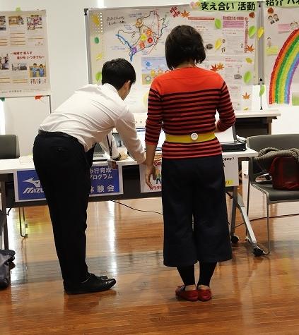 歩き方に関するデータを測定する器具を装着したまま立っている女性と測定されたデータが映しだされているモニターを机に手をついて立った姿勢で見つめる白いシャツを着た男性の写真
