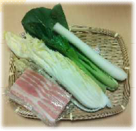 かごの上に置かれたねぎ、白菜、ベーコンの写真