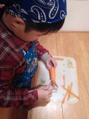 男の子がピーラーを使って人参の皮をむいているところを横から写した写真