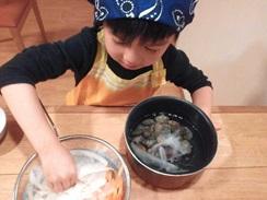 女の子がアサリが入っている鍋にボールの水に浸している大根、人参を入れている写真