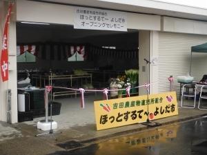 紅白のテープカットの前に「ほっとするて~よしだ市」の看板が置かれているお店の入り口の写真