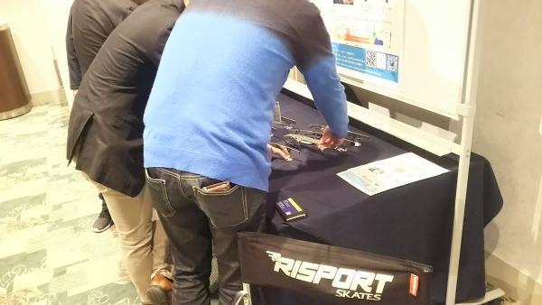 出展ブース:展示用ブレードを手に取っている成人3名の後ろ姿の写真