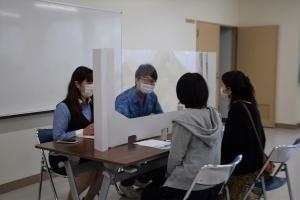 アクリル板で仕切られた机に2人1組で向かい合って面談している写真