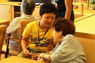年配の女性が名札を持った男の子に話しかけている写真