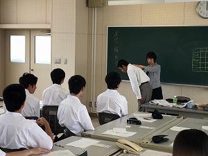 男子生徒の背中に手を当てて、お辞儀の角度を教えている女性講師と、座って聞いている生徒たちの写真