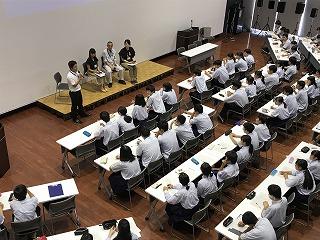 壇上に並び、話をしている職員たちと、座って聞いている生徒たちを上から撮影した写真