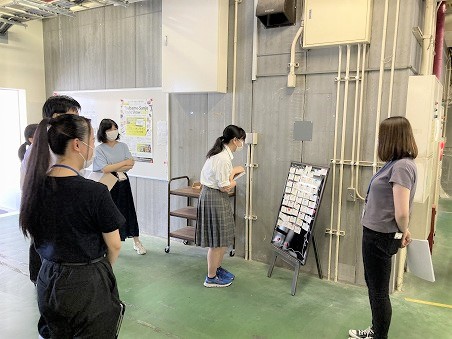女子生徒が社内の連絡ボードに貼られたコメントを読んでいる写真。