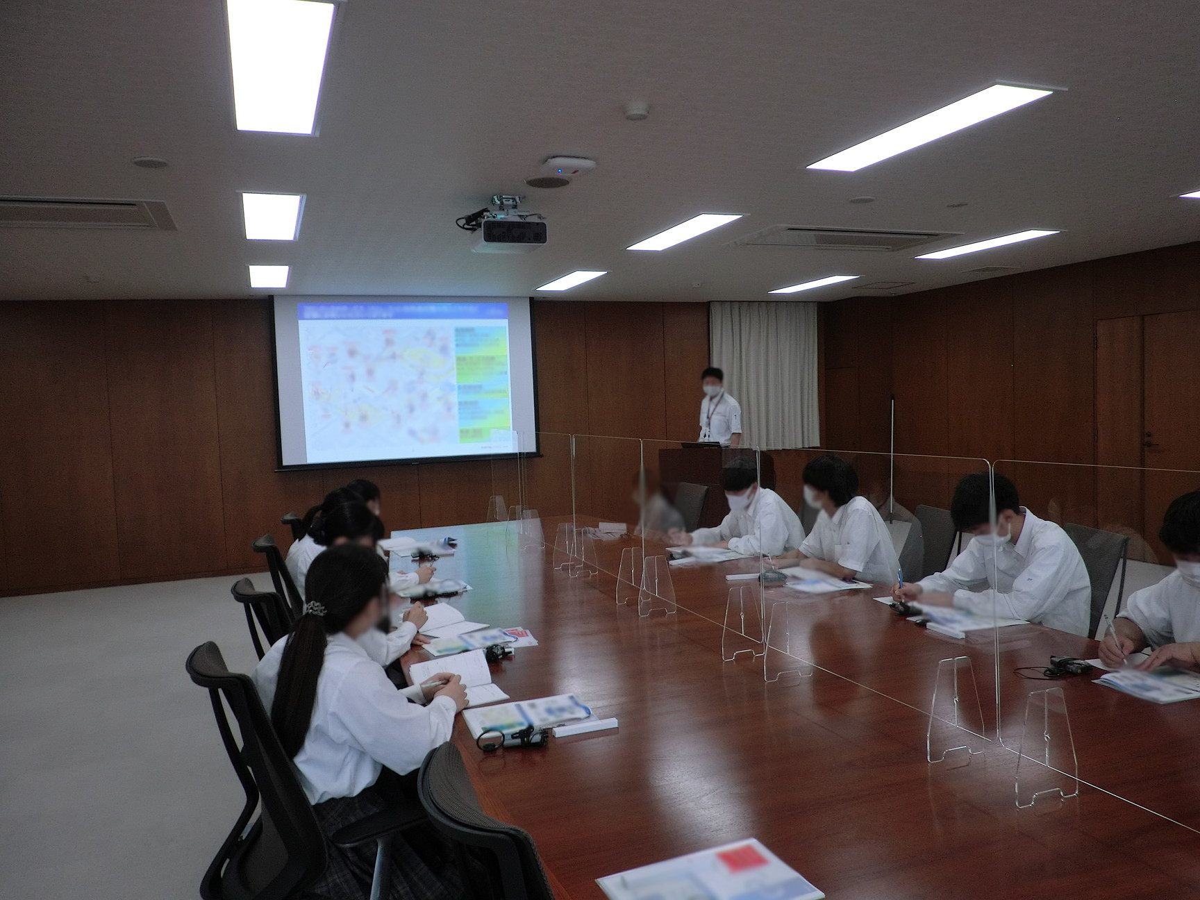 大きな会議室で、社員が生徒に会社紹介のプレゼンをしているところ