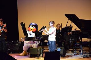 ステージの上で楽器を演奏する奏者たちとつば九郎の写真