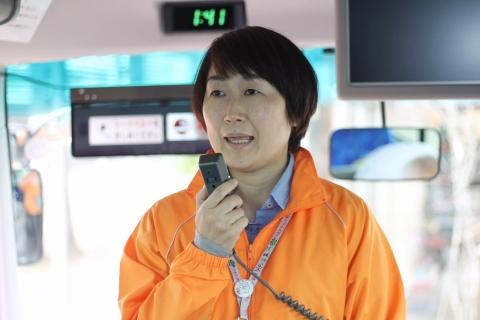 マイクを手に話すバス添乗員の写真