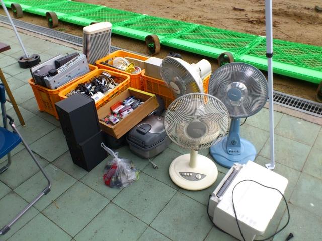 炊飯器、扇風機などの家電が屋外に並んでいる写真