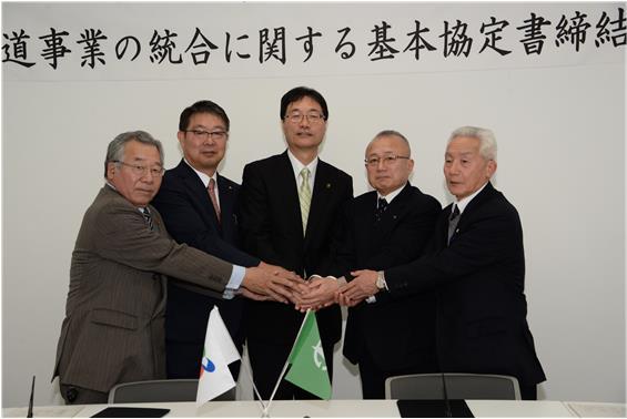 カメラに向かって手を取り合う市長と役員一同の写真