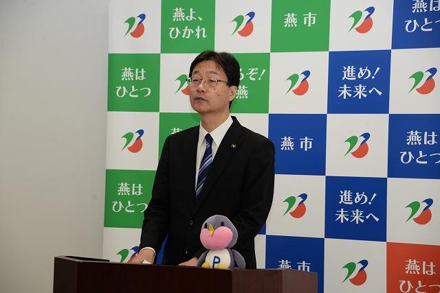 ペンギンのキャラクターのぬいぐるみと一緒に演台に立つ市長の写真