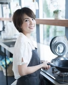 エプロンを着た女性がフライパンを持っている写真