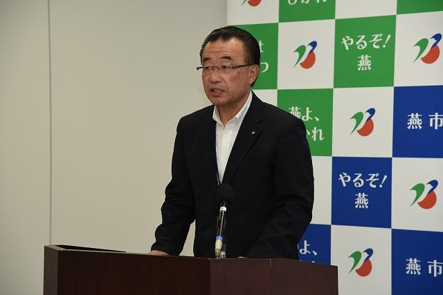 黒いスーツ姿の男性が演台で話している写真