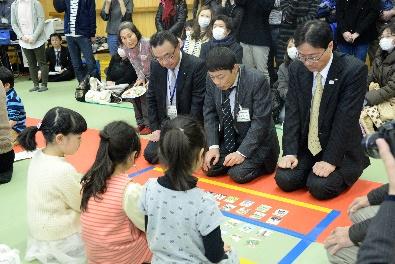 スーツを着た大人と児童が向かい合ってかるたを遊んでいる写真
