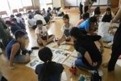 イラストの印刷された紙を広げて床に座って話をする児童たちの写真
