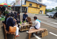 道路脇に置かれた椅子に腰かけ歓談する人たちの写真