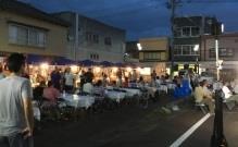簡易テーブルが置かれたマルシェ会場で、屋台の食事を楽しむ人たちの写真