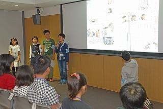 スクリーンの写真を説明している子供たちと、それを座って聞いている子供たちの写真