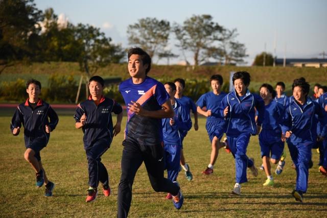 グラウンドを走る若い男性と、後を追いかける生徒たちの写真