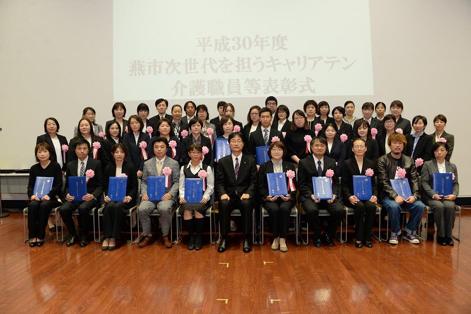 男性を中心に、表彰状を手に持った人たちが並んで写っている集合写真
