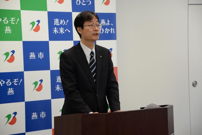 燕市のポスターの前で、演台に立って話をしている男性の写真