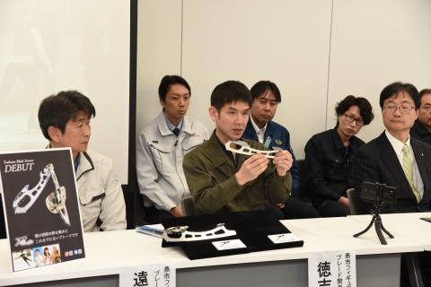 男性がフィギュアブレードの実物を手に説明をしている写真
