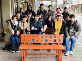 商店街のベンチに腰掛け記念撮影する人たちの写真