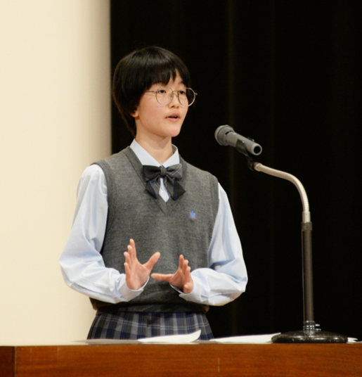 マイクの近くに立ってスピーチをする制服姿の女子生徒の写真