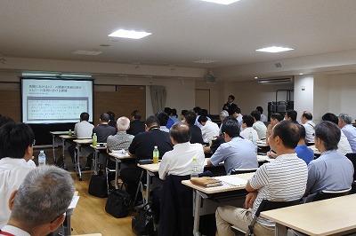 室内で着席している参加者たちがスクリーンのほうを見つめている写真