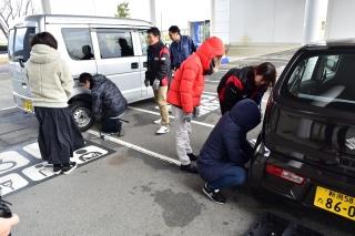駐車場に止まった車の近くに集まって講習会をしている参加者たちの写真