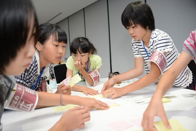 腕に腕章をつけて書き物をしている児童たちの写真