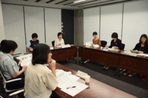 コの字に並びながら机に置いてある資料を見つつ会議に参加する女性たちの写真