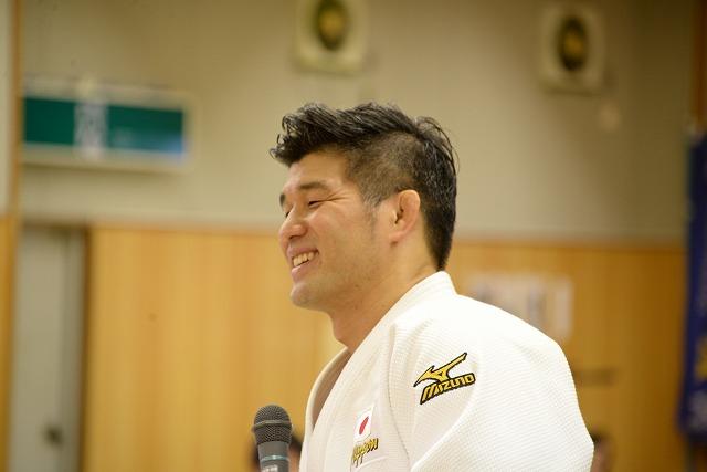マイクを持ちながら笑顔で話をしている様子の井上康生選手の写真