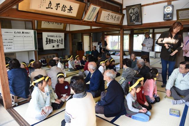 かるたに挑む黄色いはちまきを巻いた子ども達とご老人の方々の写真