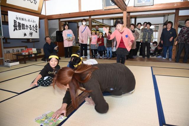 大きなかるたを一枚取った勢いで転びそうになっている女性の写真