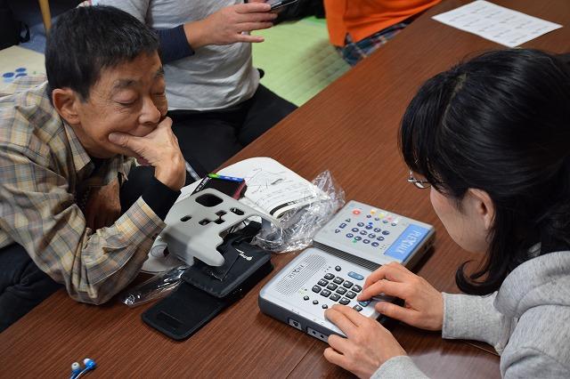 最新式のデイジー再生機を触っている女性参加者とそれを覗き込んでみている男性参加者の写真