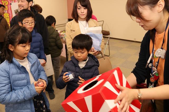 女性スタッフが持っている箱の中からガシャポンのカプセルを取り出している子どもの様子の写真