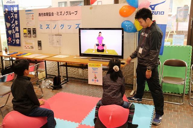 赤いバランスボールに乗っている男の子と女の子に説明をしているインストラクターの様子の写真