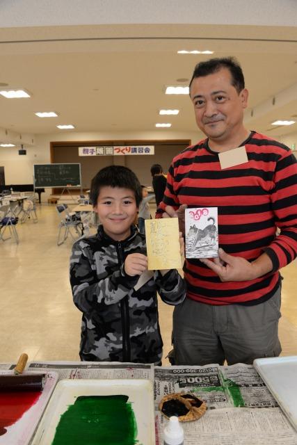 出来上がったハガキサイズの作品を持ち、笑顔の男の子と男性の写真