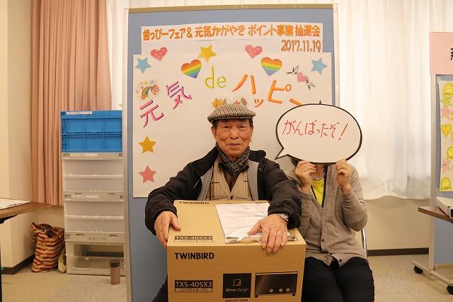 当選した景品のトースターを抱えて椅子に座っている男性の写真