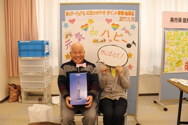 当選した掃除機を抱えて椅子に座っている男性と「がんばったぞ!」と書かれた手書きの吹き出しを持った方の写真